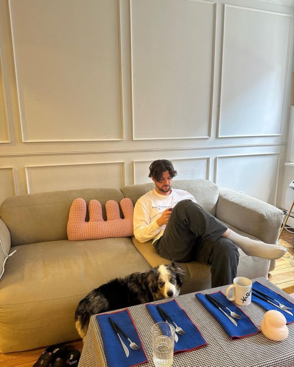 Na imagem com cor, um homem sentando em um sofá cinza - Metrópoles