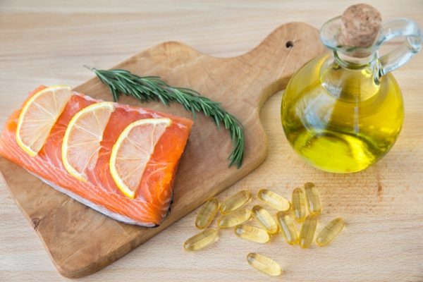 Foto mostra salmão servido ao lado de azeite e cápsulas de omega-3