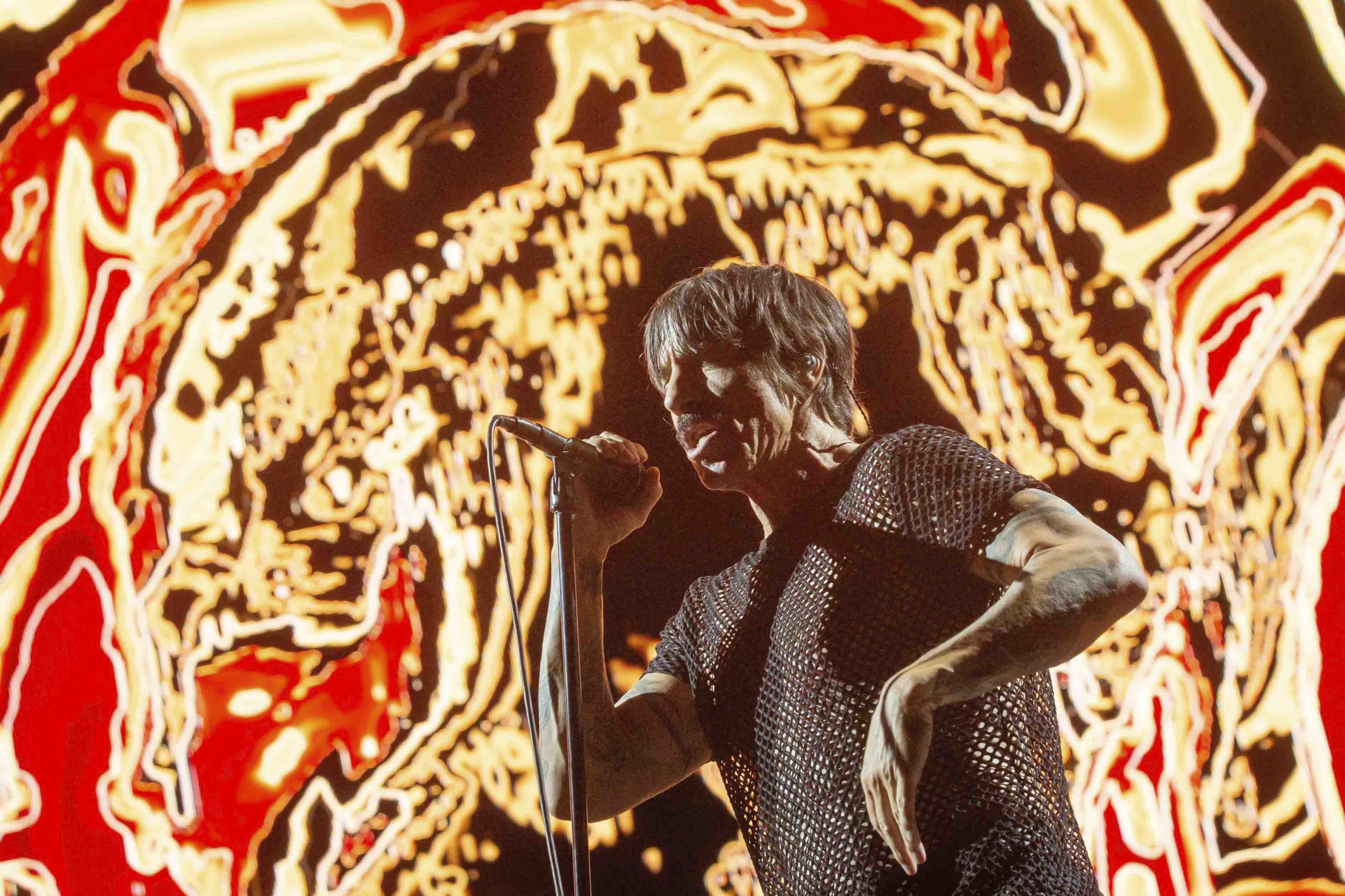 Foto colorida de Anthony Kiedis cantando com fundo vermelho e dourado - Metrópoles