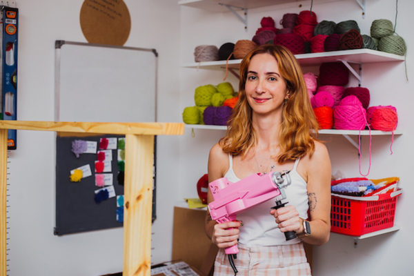 Na imagem com cor, uma mulher branca, ruiva, com roupas claras, usando uma pistola de tuffiting - Metrópoles