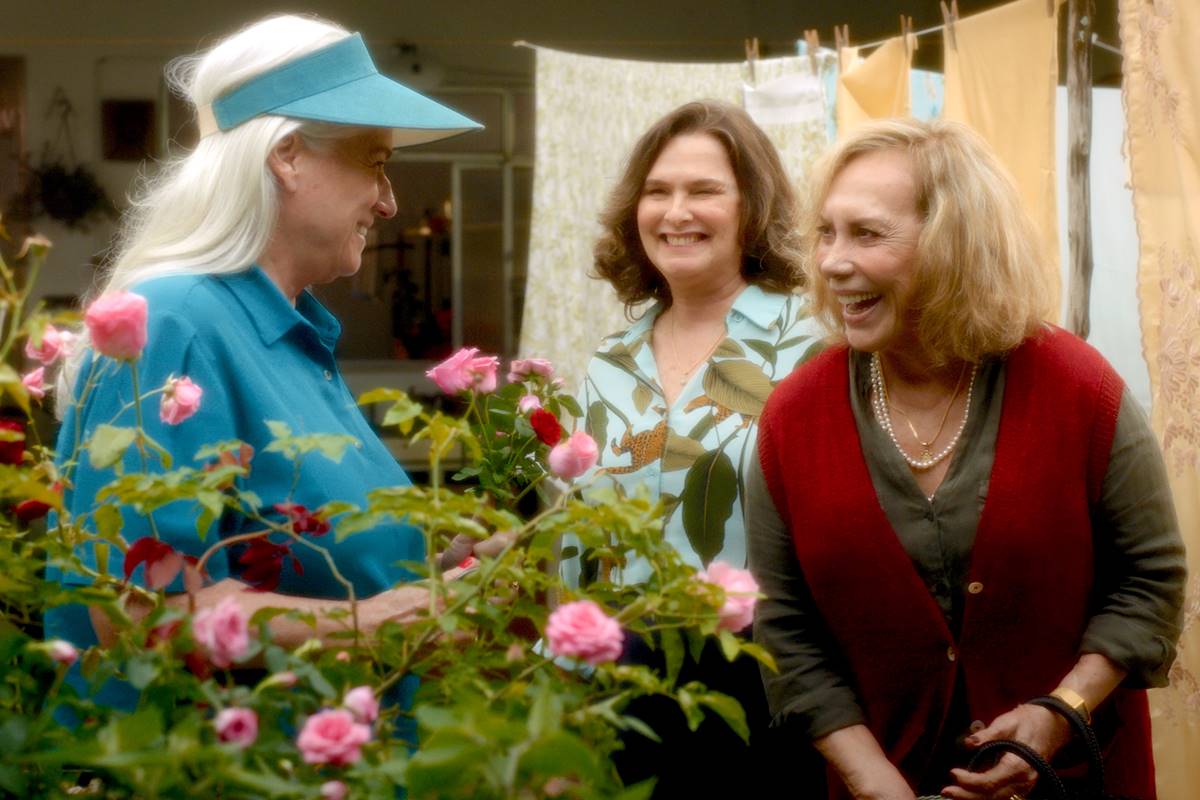 foto colorida de vera holtz de blusa e chapeu azuis, sorrindo para arlette sampaio, que veste camisa estampada e colete vermelho e louise cardoso de blusa estampada sorrindo ao fundo - metrópoles