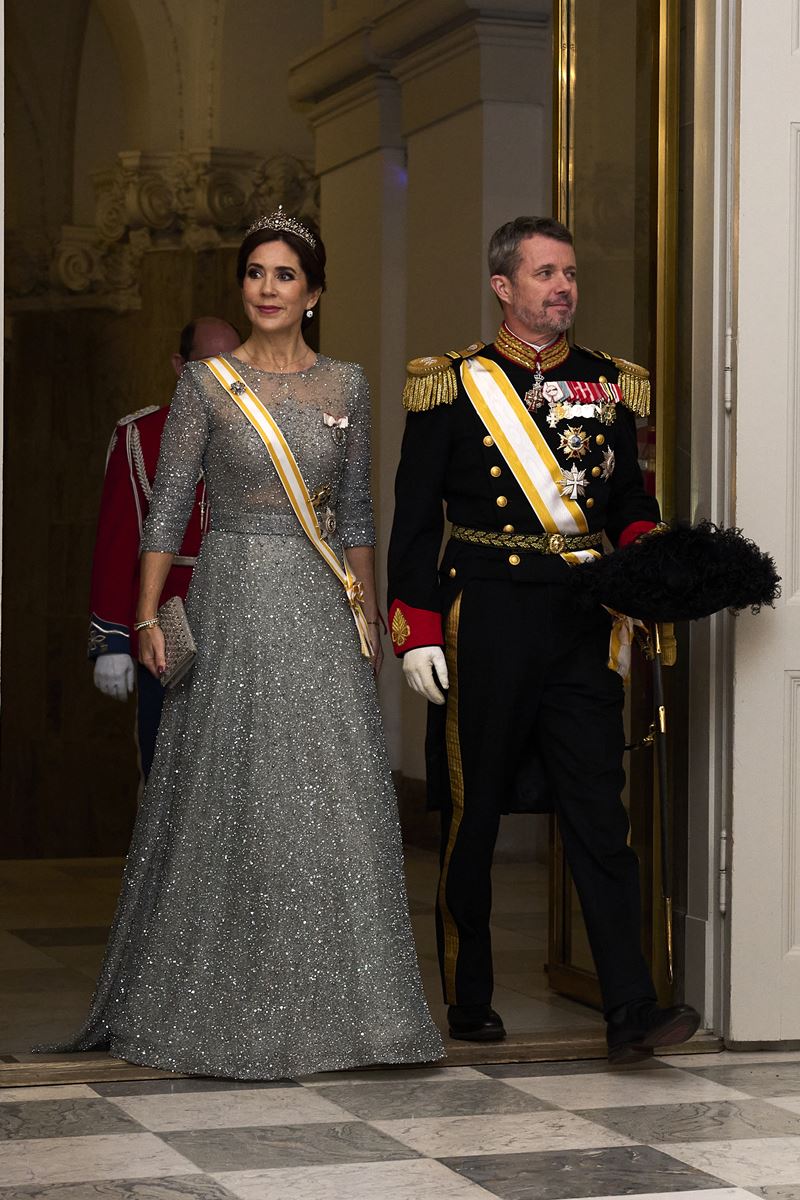 Foto colorida de mulher, com cabelo preso, tiara, faixa dourada e vestido longo br