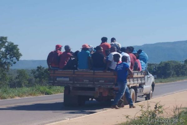 Pessoas amontoadas em pau-de-arara pela estrada. Na imagem é possível ver que tem pessoas em pé no local 