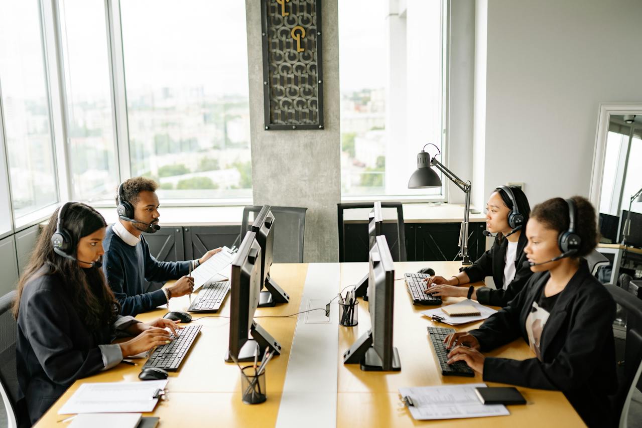 Quatro pessoas trabalhando sentadas em uma mesa de escritório com computadores - Metrópoles