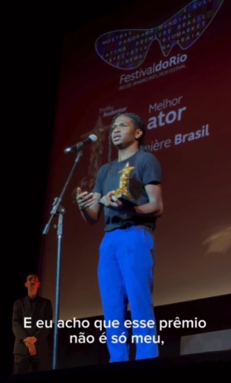 Foto colorida do ator Kauan Alvarenga com calça azul e blusa preta durante premiação no 25º Festival do Rio