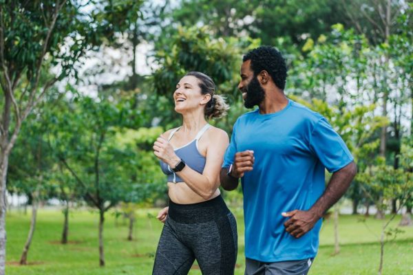 Foto colorida de um casal correndo no parque sorrindo - Metrópoles