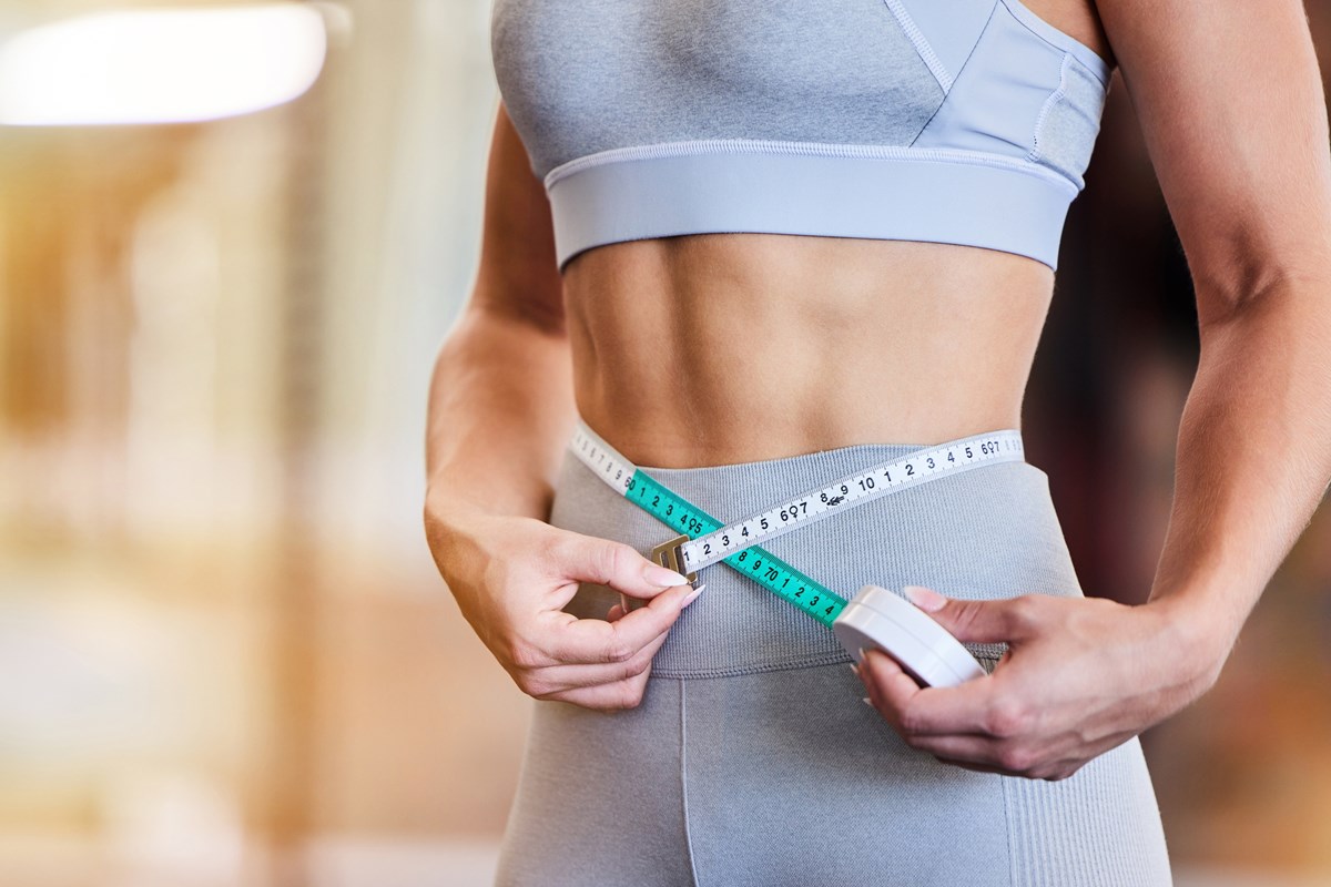 Foto colorida de abdômen feminino. Mulher está com fita métrica medindo a barriga - Metrópoles