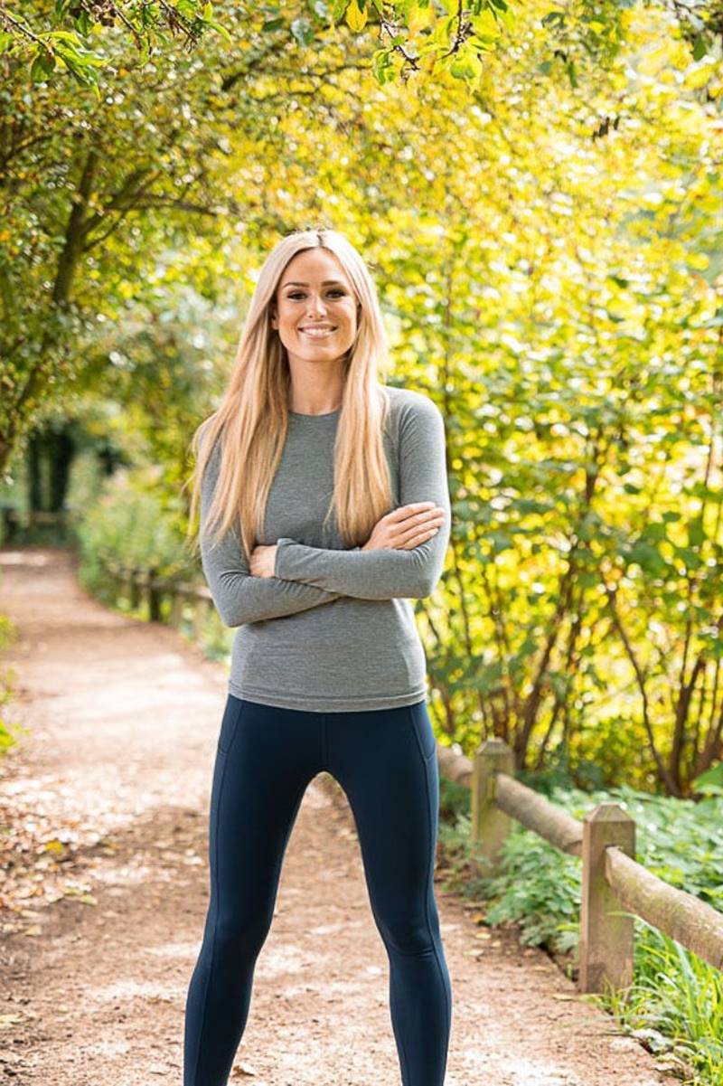 Foto colorida de mulher loira, em pé, com roupa de academia em um parque - Metrópoles