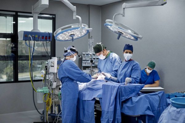Imagem colorida de sala de cirurgia com médicos em volta de paciente desacordado - Metrópoles