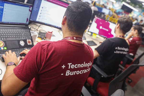 Fotografia colorida mostrando três homens de costas mexendo em computadores-Metrópoles