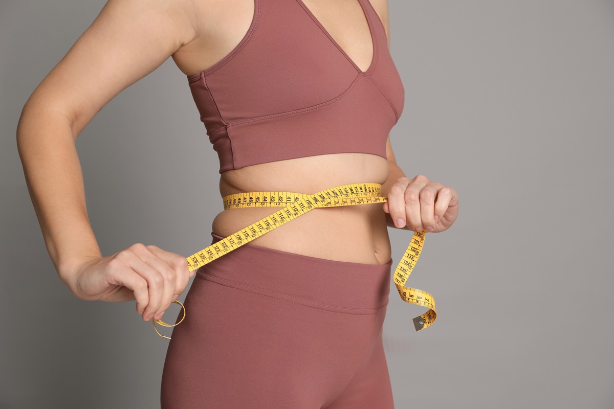 Foto colorida de mulher com fita métrica na barriga. Ela usa um cropped e uma legging - Metrópoles - emagrecer