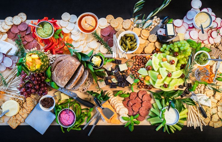 Foto colorida mostra mesa servida com frutas, vegetais e pães dispostos de forma estética