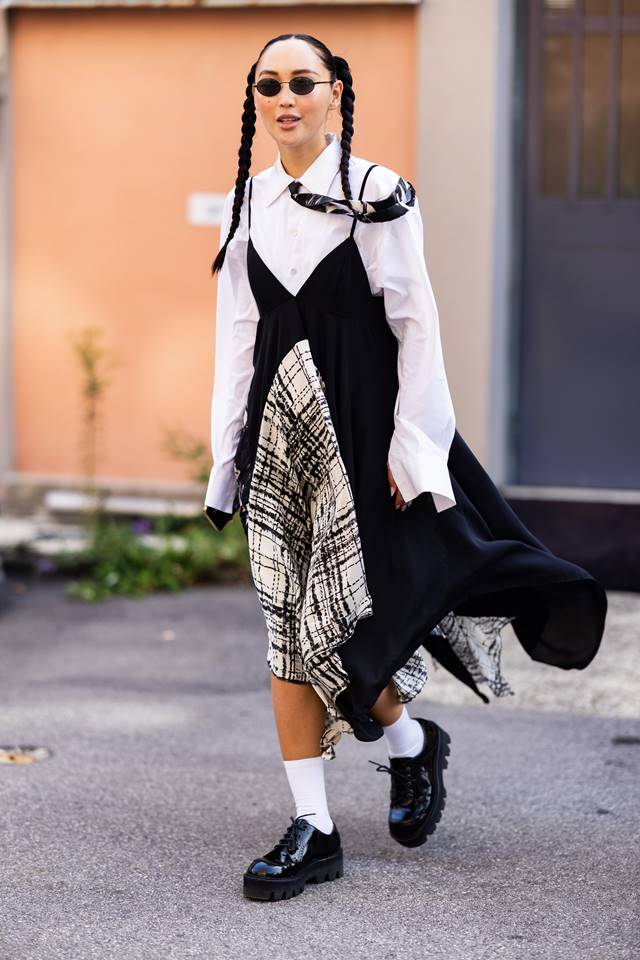 No street style, mulher usa vestido estampado por cima de camiseta branca. Nos pés, meia branca e sapato preto fechado - Metrópoles