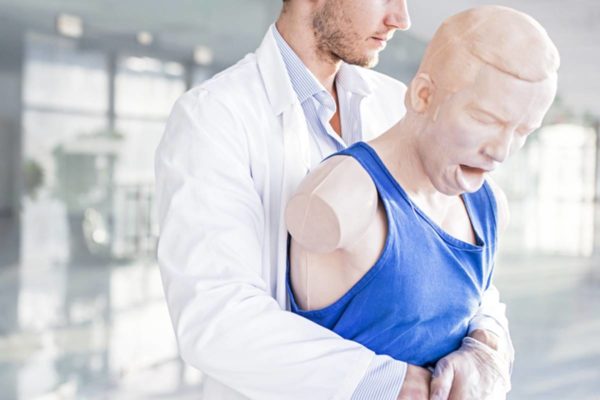 Imagem colorida de médico aplicando a manobra de heimlich em boneco de treino