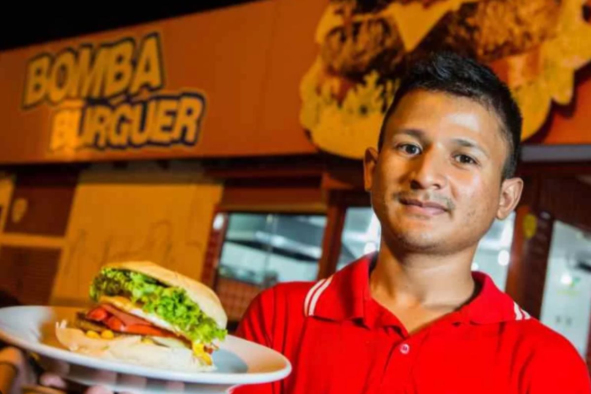 Foto colorida de um homem segurando um hambúrguer - Metrópoles