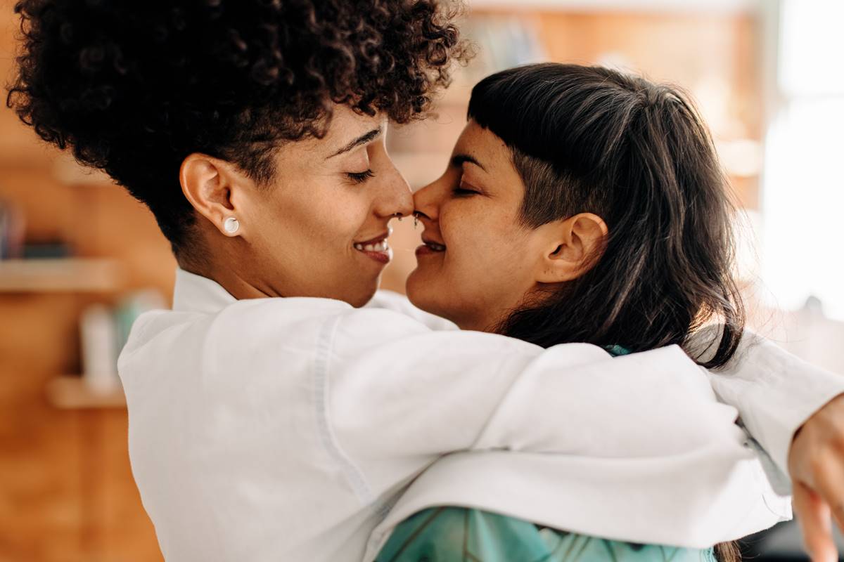 Foto colorida de um casal com os narizes encostados olhando uma para a outra e sorrindo - Metrópoles