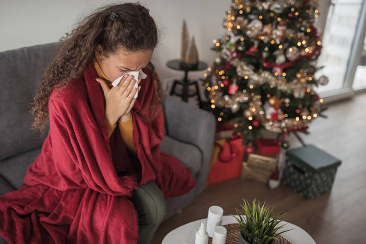Foto ilustrativa de mulher com alergia com lenço de papel no nariz em casa com decoração de Natal - Metrópoles