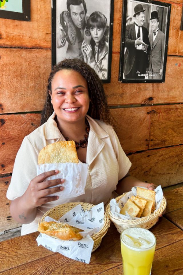 Foto colorida de uma mulher comendo pastel - Metrópoles