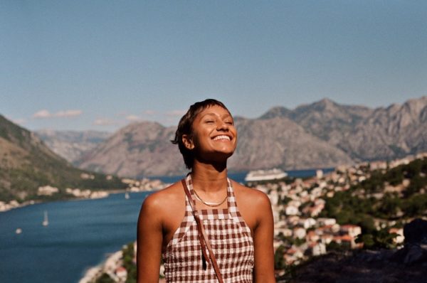 Foto colorida mostra mulher jovem parda sorrindo e tomando sol