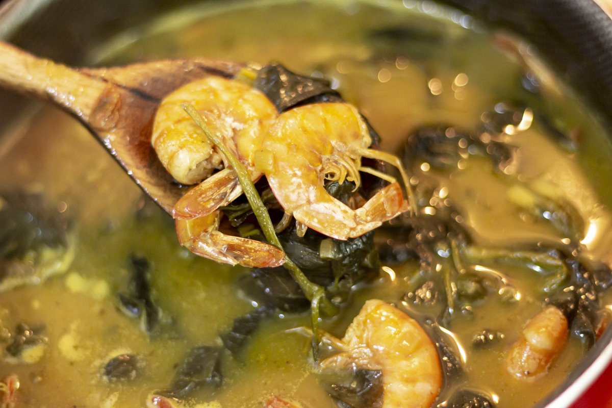 Foto de ingredientes do caldo de tacacá em uma colher de pau. Atrás, há uma panela - Metrópoles