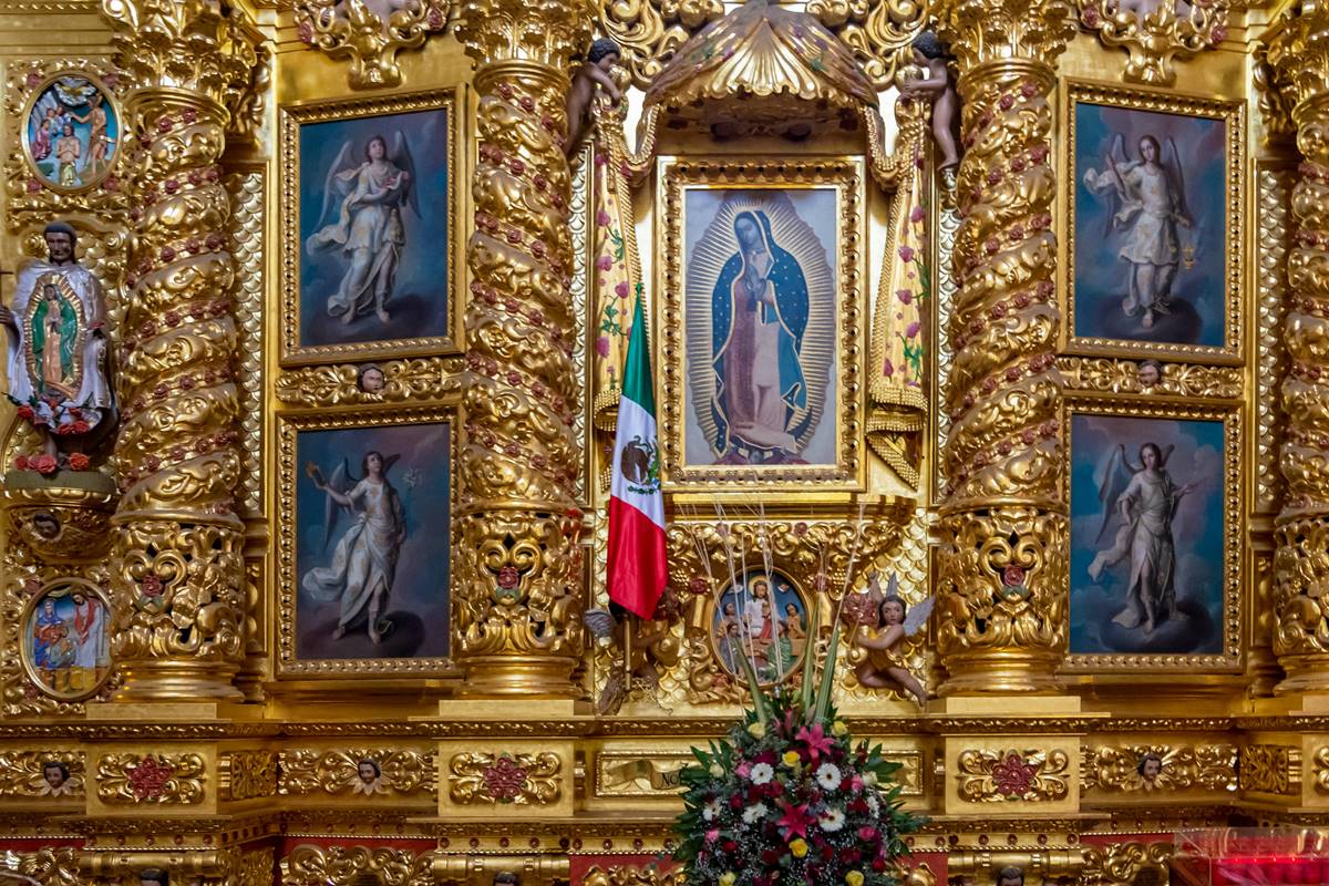 Foto colorida de imagem de Nossa Senhora de Guadalupe perto de uma bandeira do México - Metrópoles