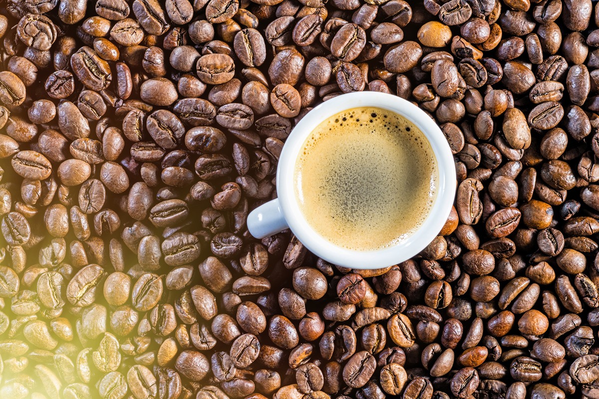 Xicara de café sobre vários grãos marrons da bebida - Met´ropoles