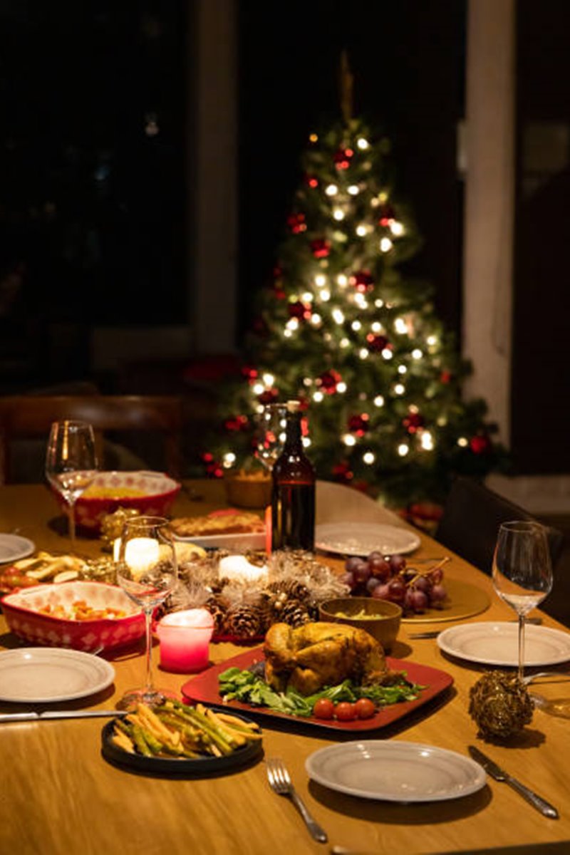 Mesa de natal decorada e cheia de comidas; árvore no fundo