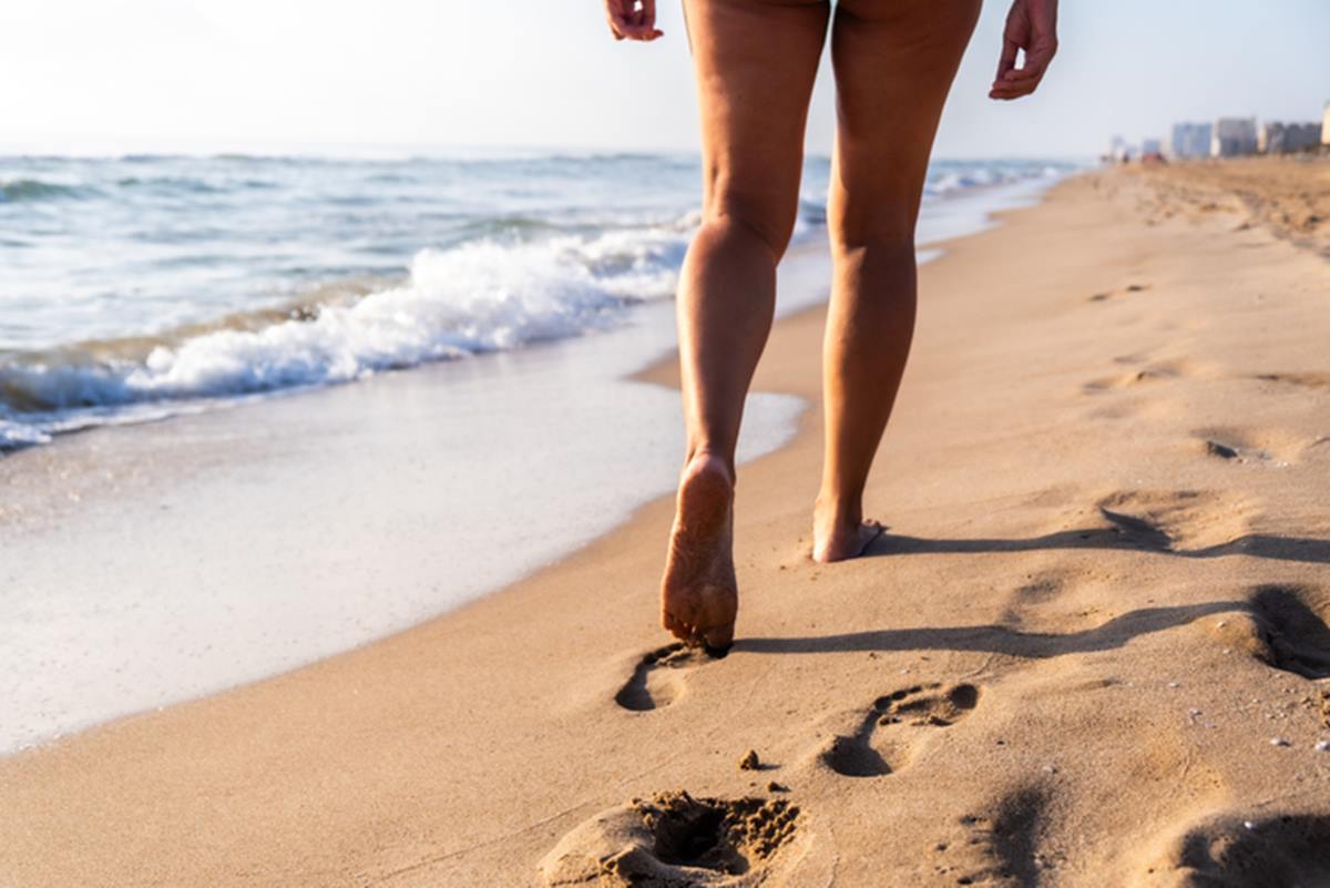 Pernas de mulher caminhando na praia - Metrópoles