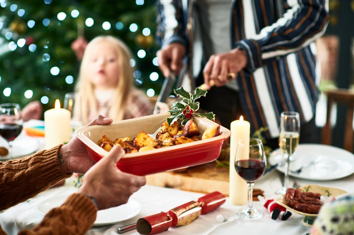 Mãos cortando batatas assadas em travessa durante ceia de Natal