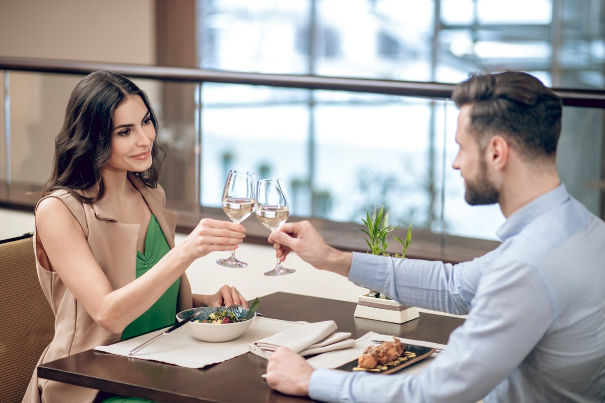 No restaurante, um casal jantando no restaurante e fazendo um brinde. Eles são brancos e de cabelos pretos - Metrópoles