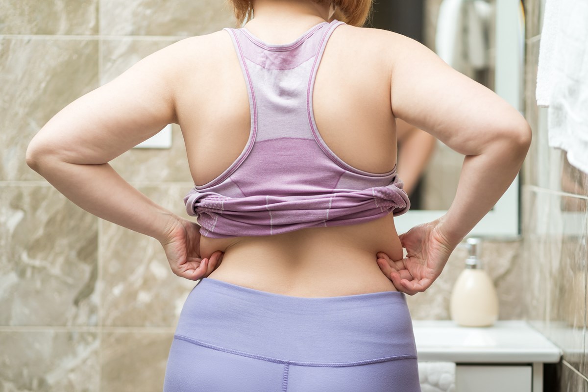 Foto de mulher se olhando no espelho. Ela está de costas e pegando em gordura localizada - Metrópoles