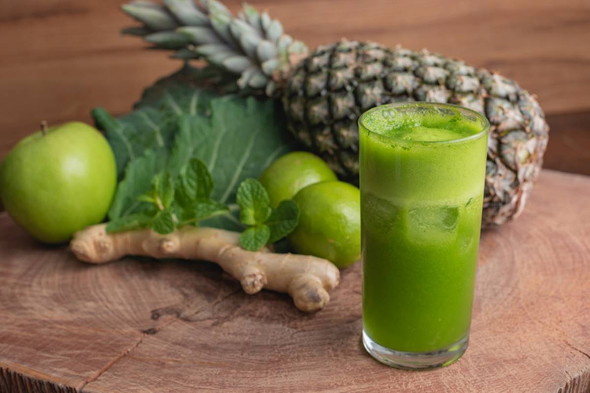 Copo de suco verde à frente de abacaxi, gengibre e maçã verde