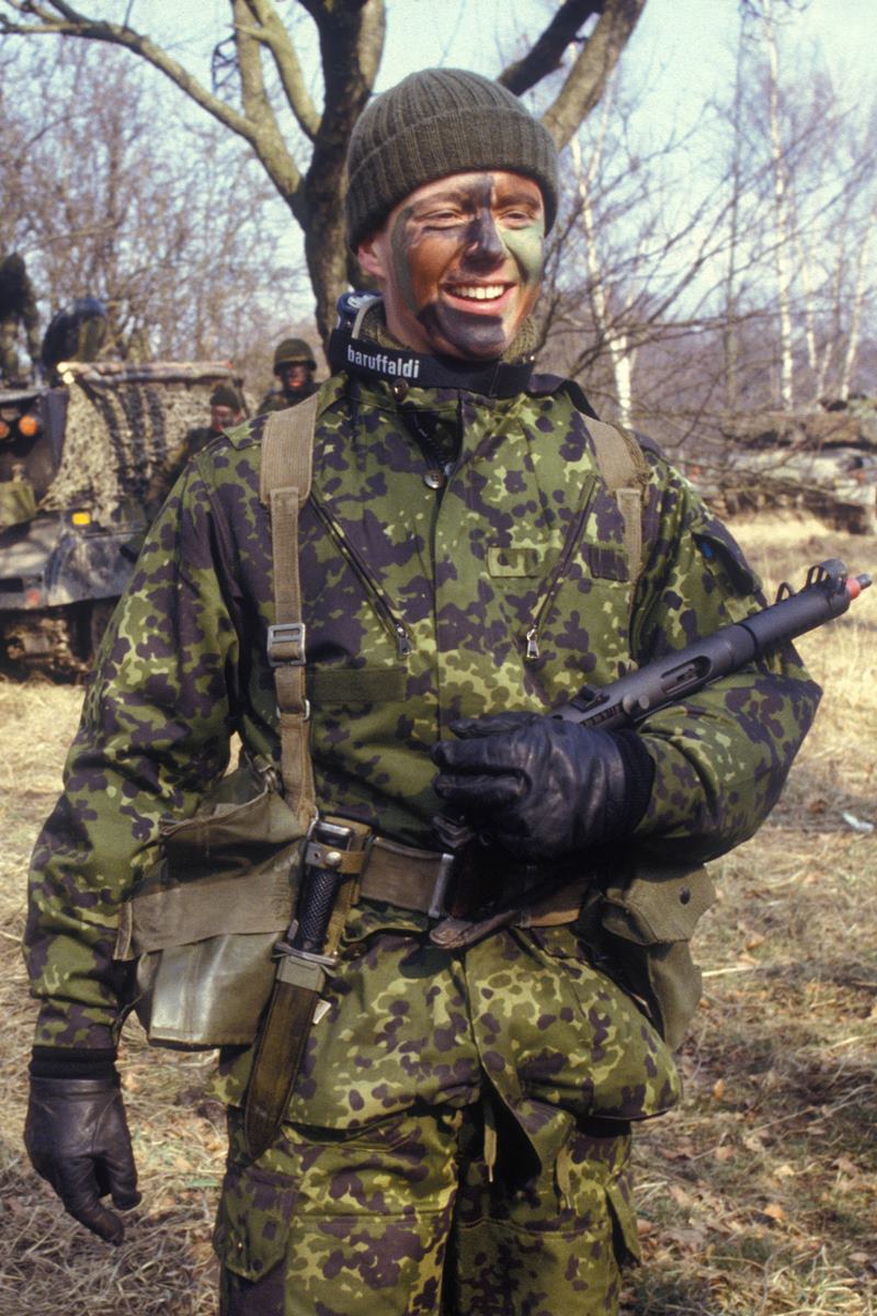 Foto colorida de homem com roupa militar. Ele segura uma arma e está com o rosto pintado - Metrópoles