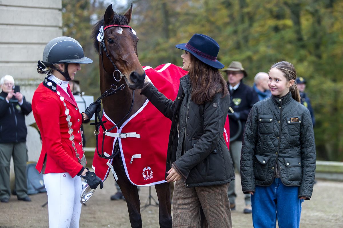 Foto colorida de mulher pegando em cavalo ao lado de menino, vestida com roupas de frio. Ao lado delas, tem uma amazona - Metrópoles