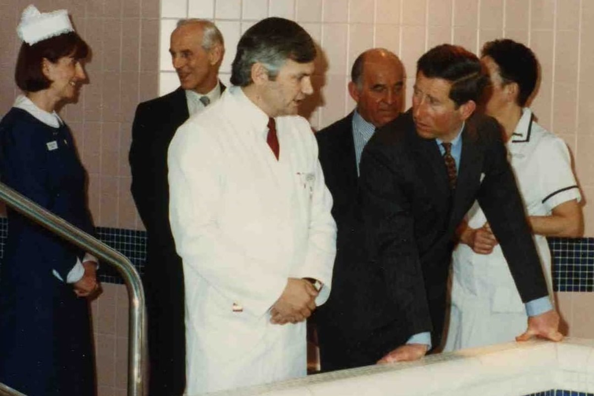 Foto de uma mulher com vestes de enfermeira, homens com terno e um deles está de jaleco. Todos estão conversando - Metrópoles