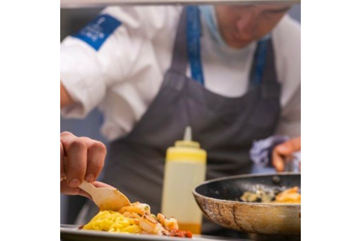 Foto de chef montando prato. Ele está segurando uma frigideira - Metrópoles