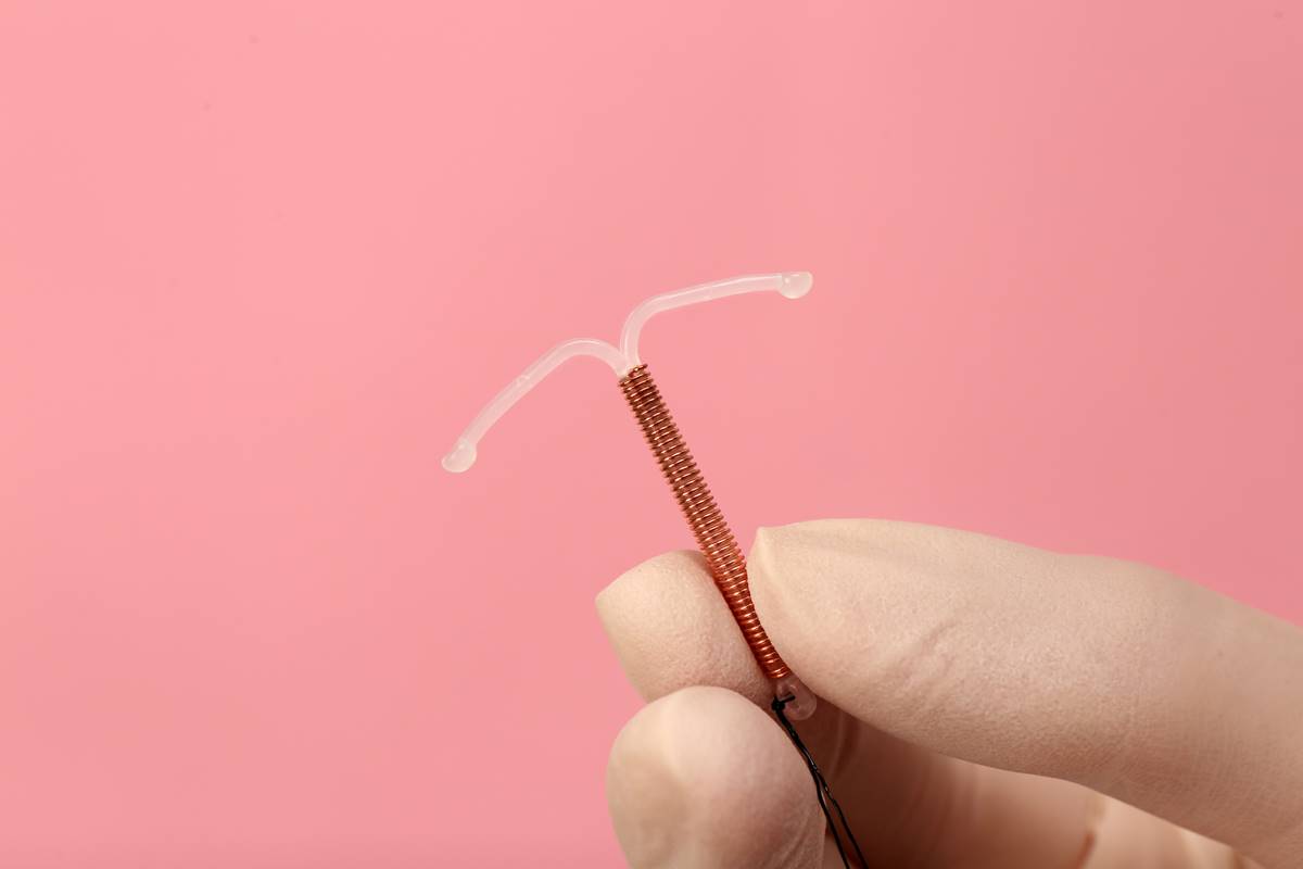 Foto colorida de uma mão com luvas brancas segurando um diu de cobre em um fundo cor-de-rosa - Metrópoles