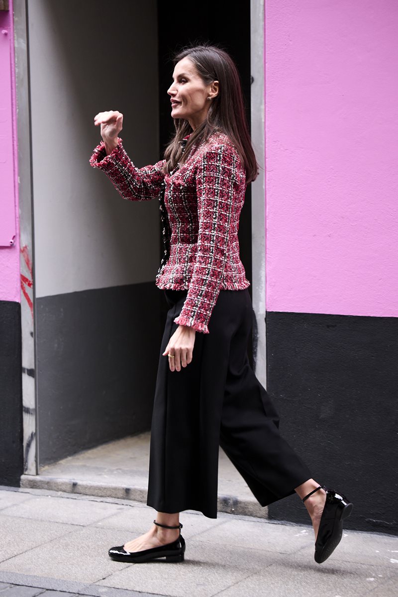 Foto de mulher, com cabelo castanho. Ela está com um casaco de tweed vermelho, calça preta e sapato preto. Ela está caminhando - Metrópoles