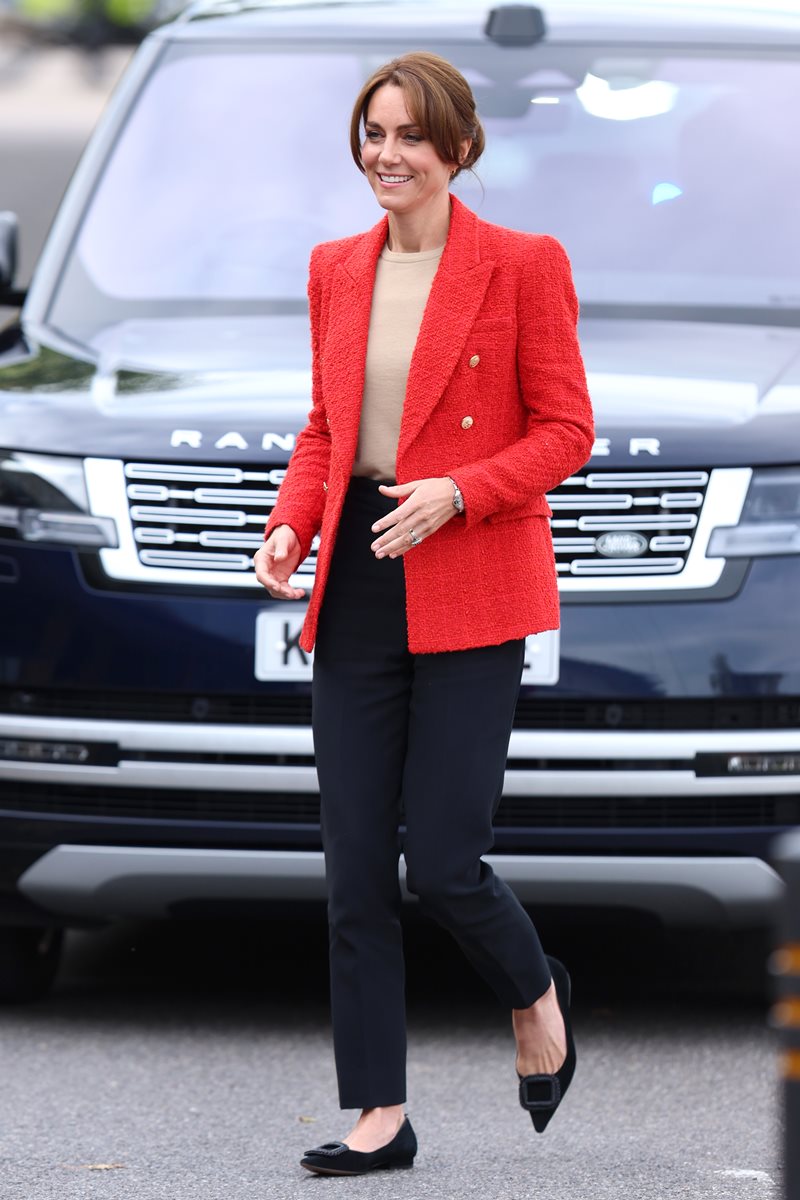 Foto de mulher com cabelo preso, blazer vermelho e calça preta. Ela está andando - Metrópoles