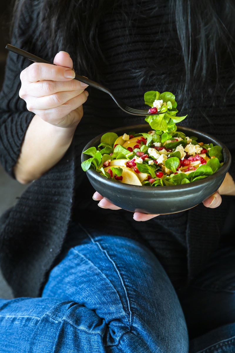 Foto colorida de mulher com garfo em salada com sementes de romã - Metrópoles