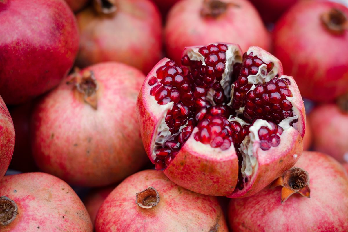 Foto colorida de romãs inteiras com uma fruta cortada em cima - Metrópoles