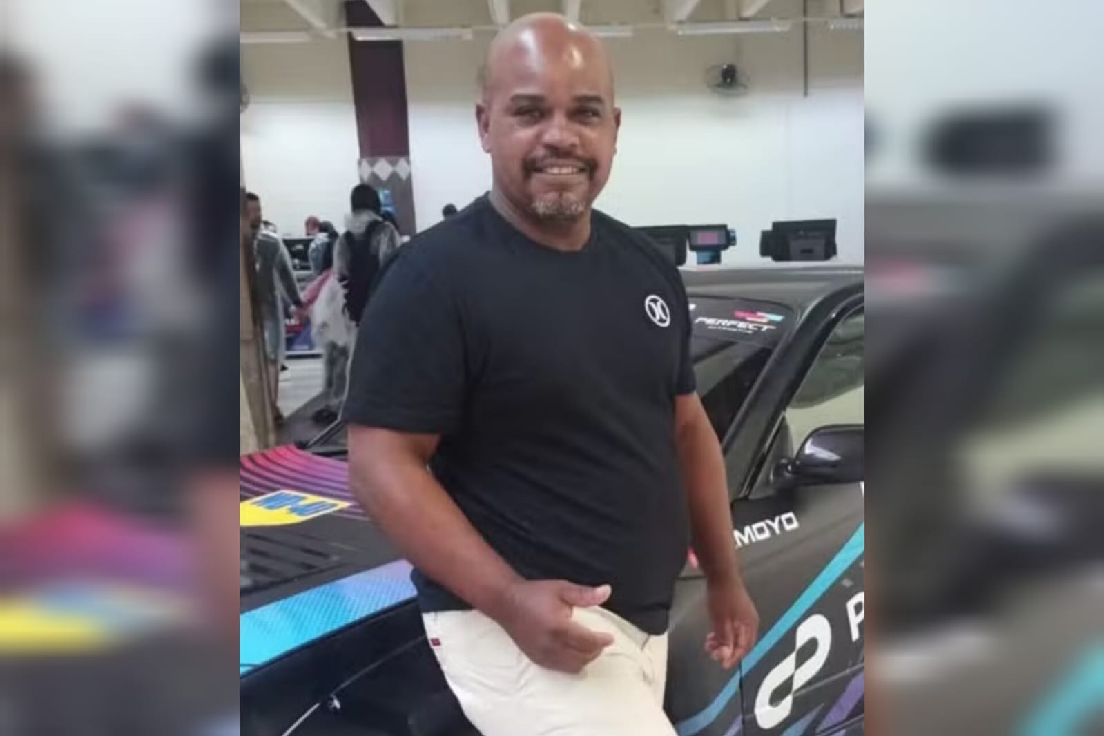 Foto mostra homem negro acenando para a câmera e sorrindo encostado em um carro. Ele é Magno Lopes, que morreu após comer um baiacu envenenado