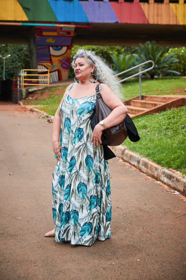 Mulher com vestido branco estampado com folhas azuis. Grafites da Galeria dos Estados fazem o fundo da imagem.