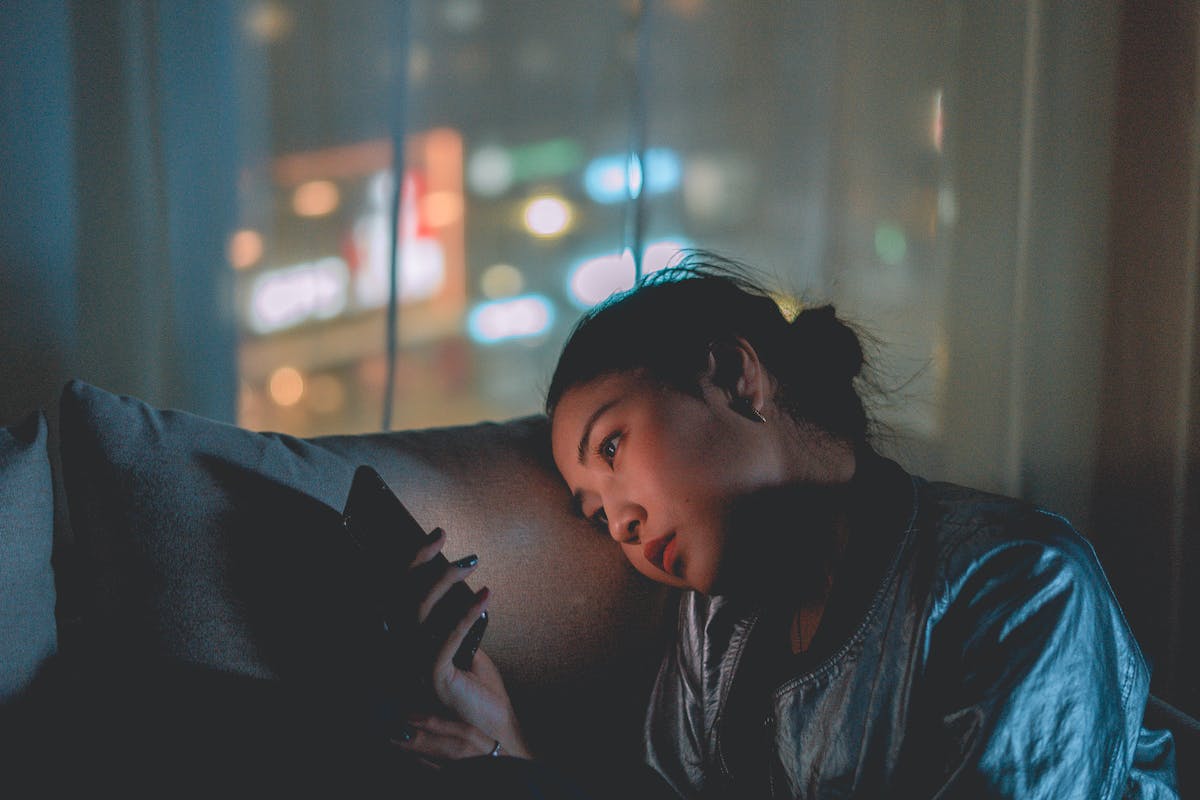 Jovem mulher asiática mexendo em celular no escuro - Metrópoles