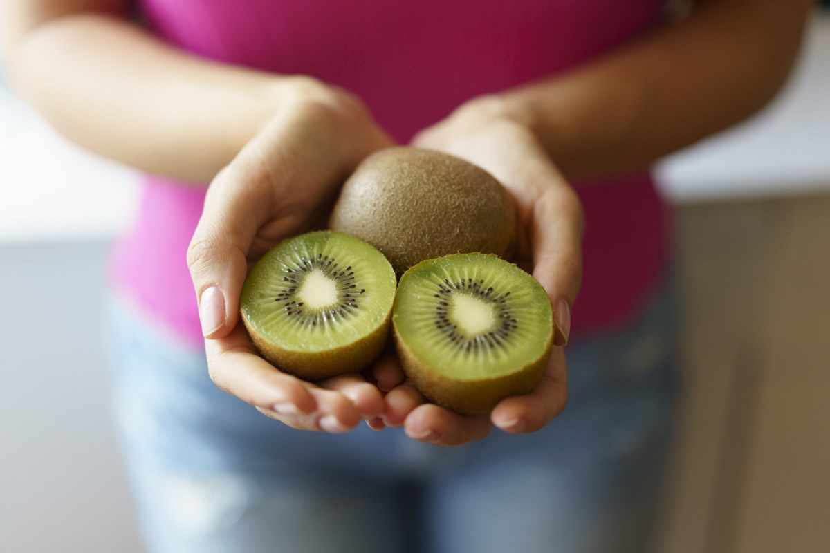 Um kiwi, fruta com casca marrom e interior verde, fechado e um cortado no meio