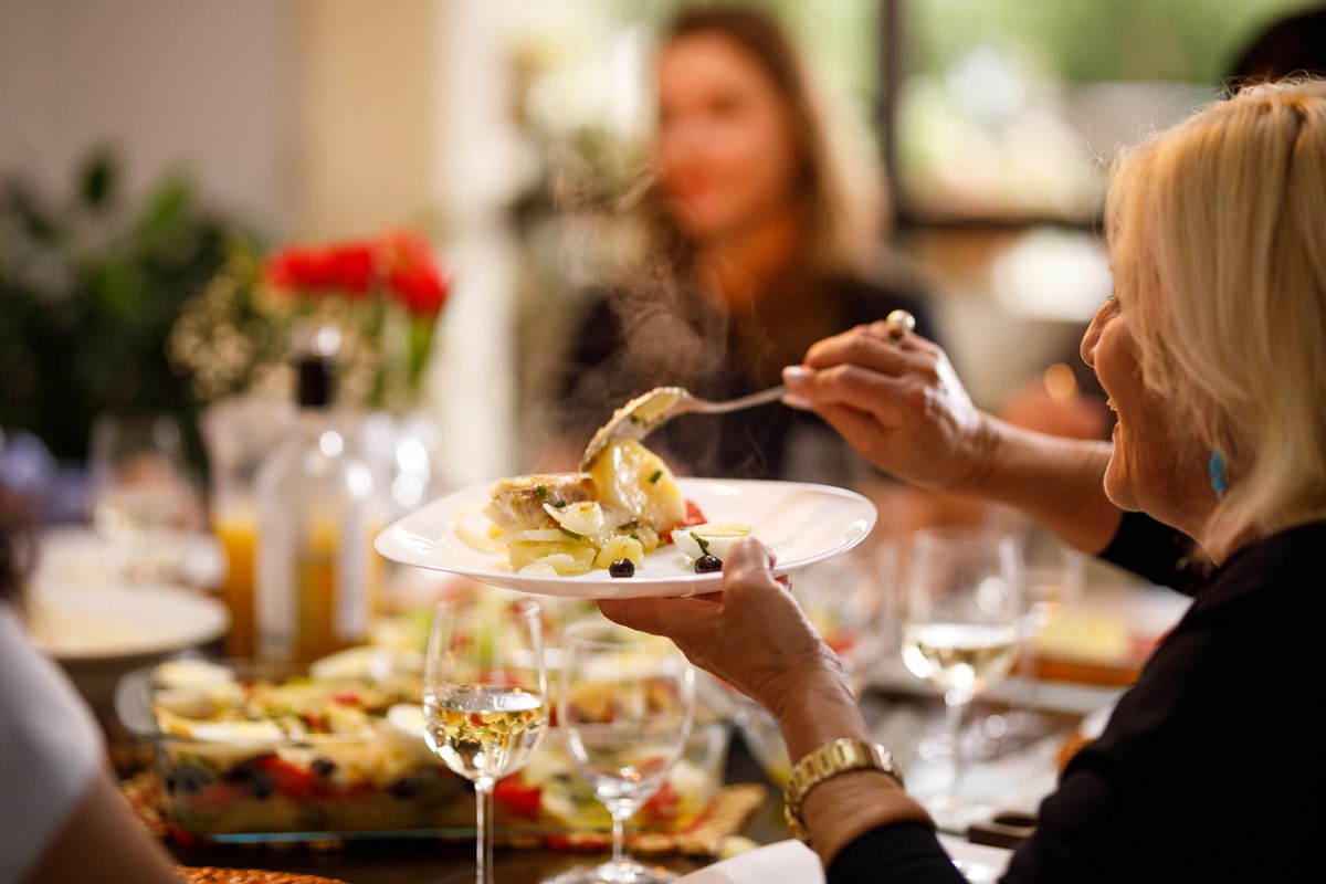 Mulher servindo refeição de bacalhau em mesa com outras pessoas - Metrópoles