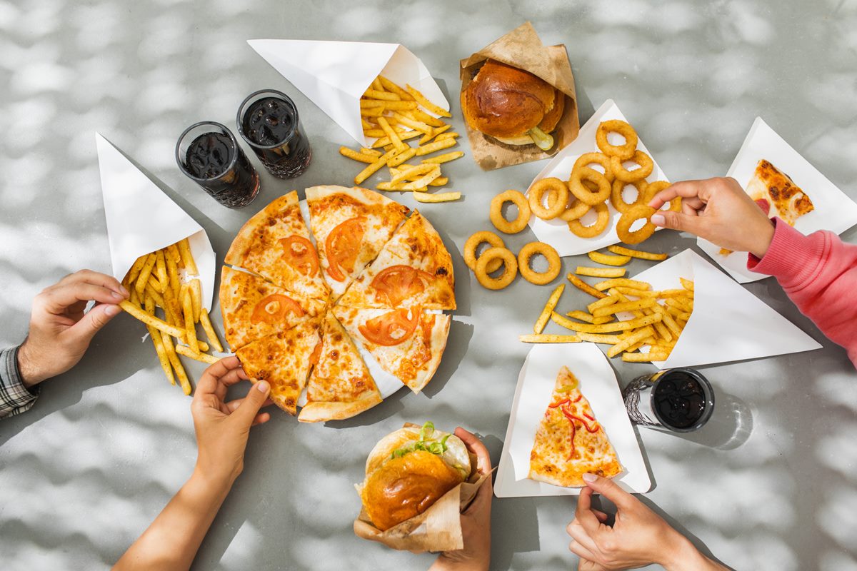 Alimentos na mesa, como pizza, batata frita e refrigerantes