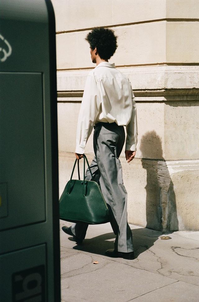 Em campanha de moda, homem anda pela rua usando roupa social e segurando bolsa verde - Metrópoles