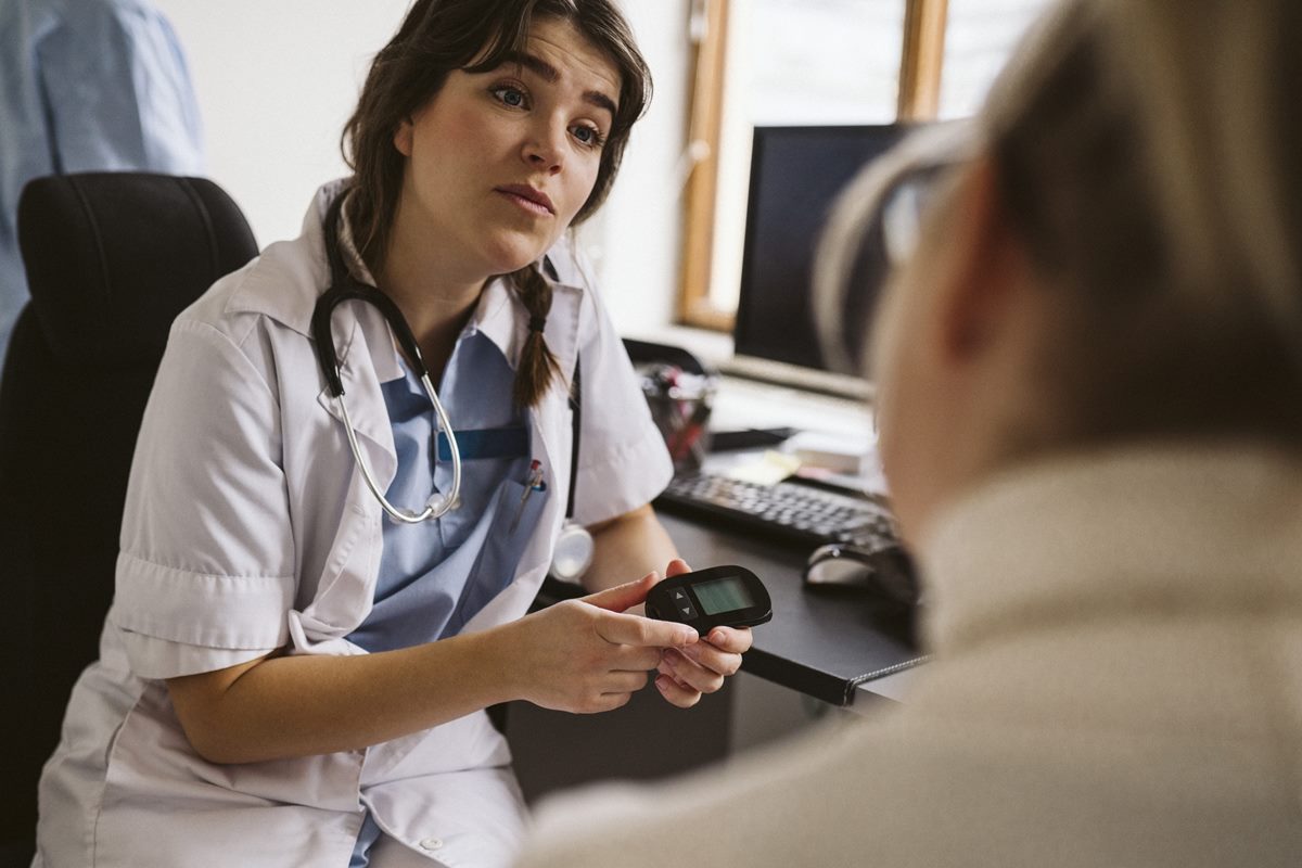 Médica mulher com um medidor de glicose na mão atendendo um paciente 