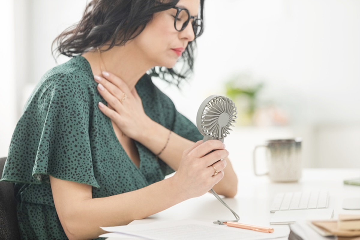 Imagem ilustrativa de melhor na menopausa se refrescando com ventilador na mão - Metrópoles